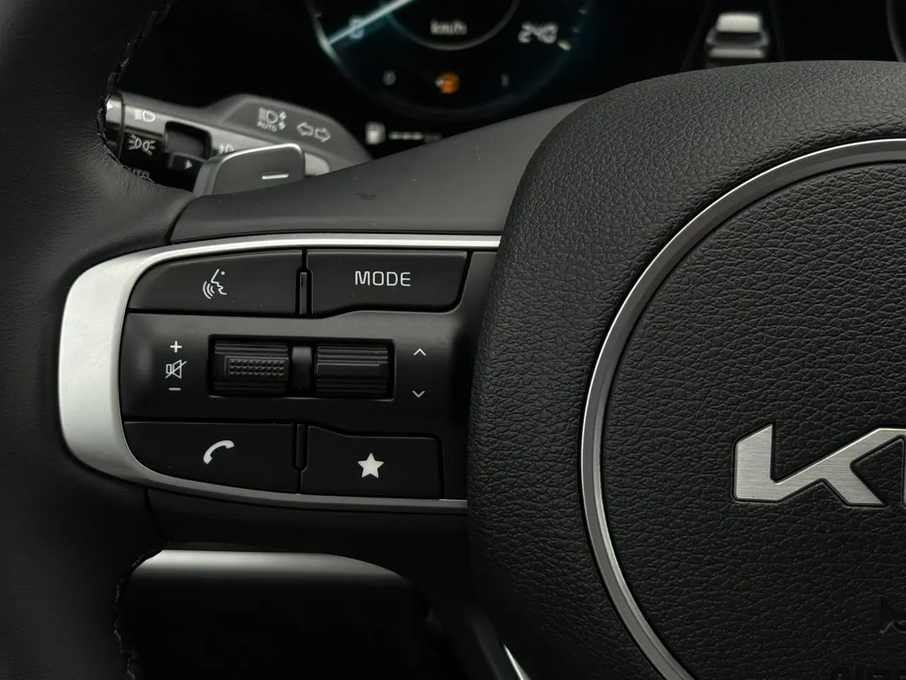 Gros plan sur les commandes gauche du volant cuir noir du Kia Sportage 2025, avec boutons multifonctions et logo central.