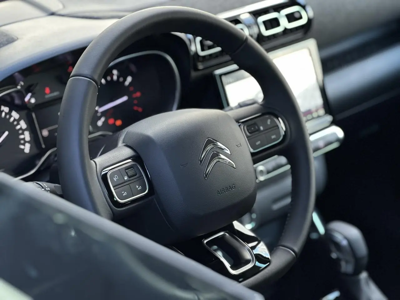 Vue rapprochée du volant noir de la Citroën C3 Aircross 2024 avec commandes intégrées et tableau de bord en arrière-plan.