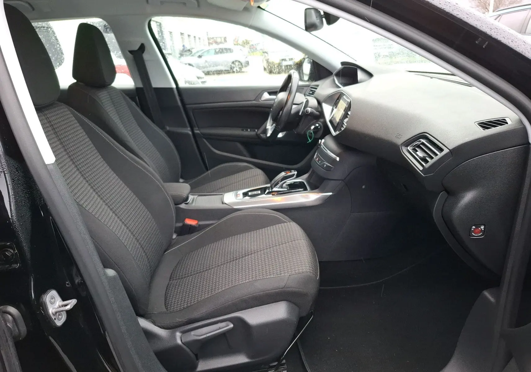 Vue intérieure côté gauche de la Peugeot 308 SW noire, montrant les sièges avant et le tableau de bord moderne.