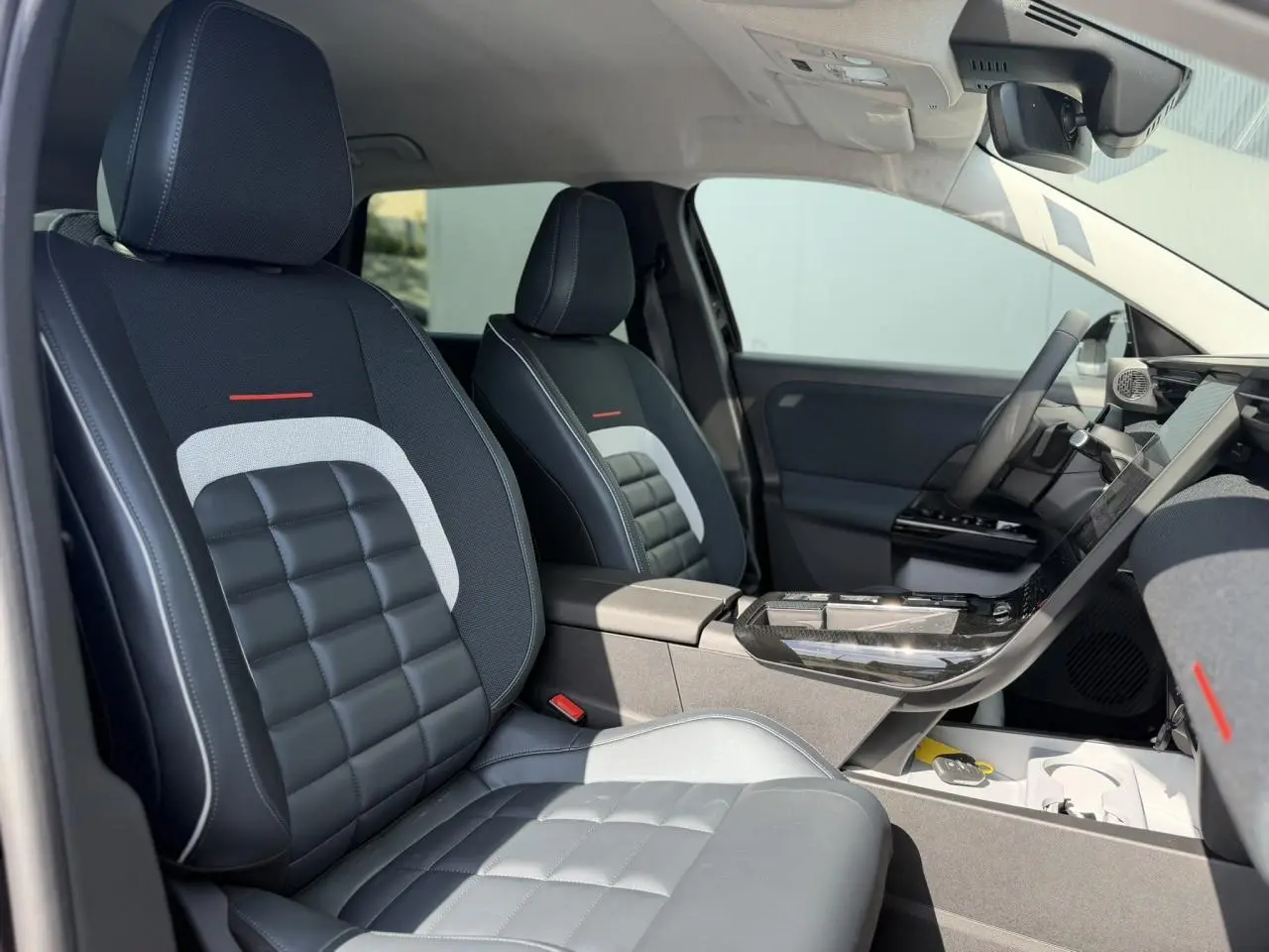 Intérieur de la Citroën C5 Aircross 2026, vue côté droit sur sièges noirs et gris avec surpiqûres blanches et accoudoir central.