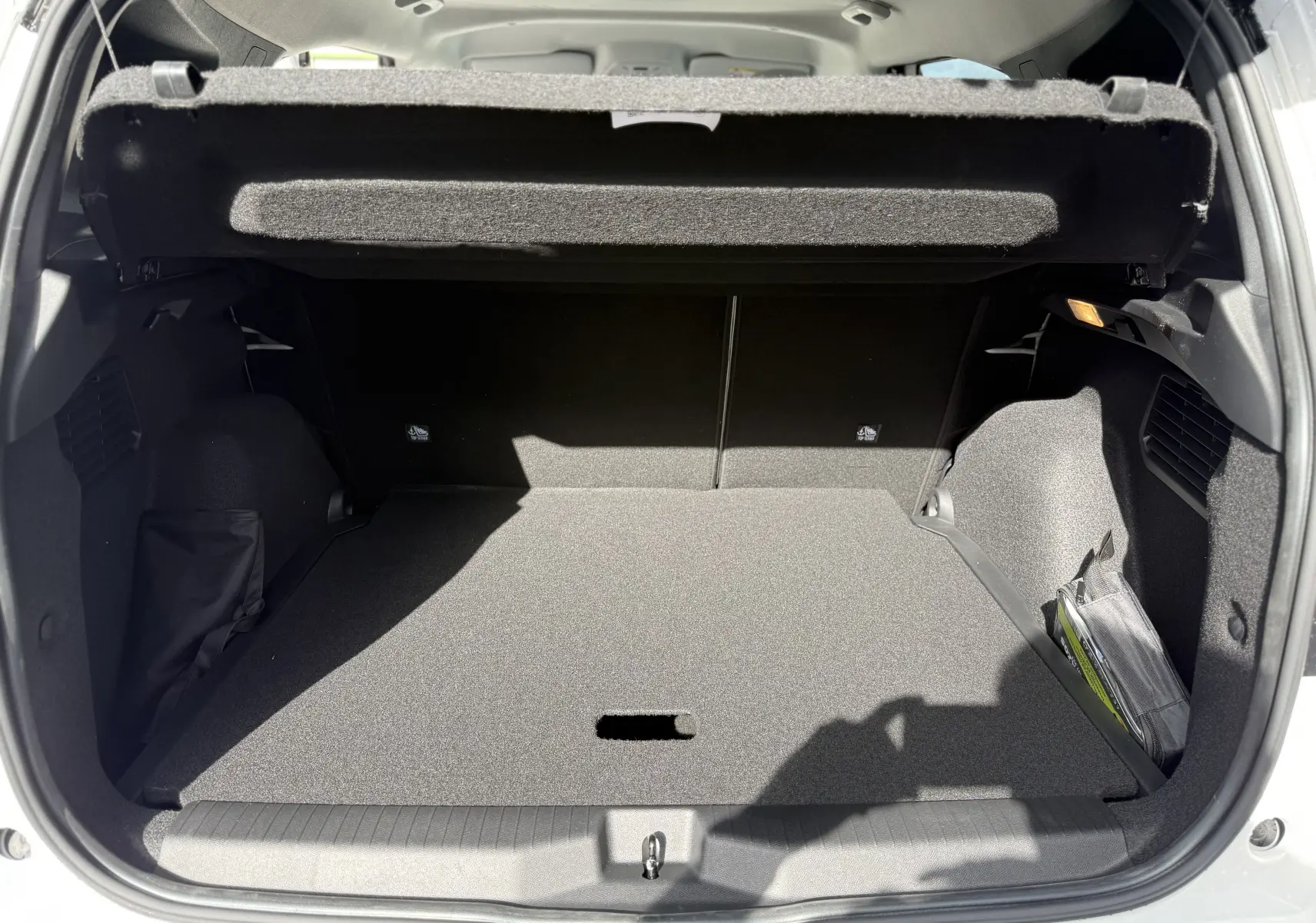 Coffre ouvert vu de l'arrière d'une Citroën C3 Aircross blanc banquise avec cache-bagages relevé et intérieur noir.
