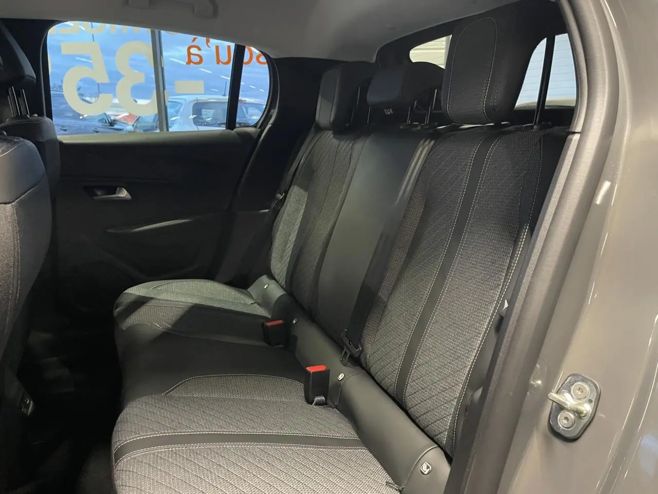 Vue intérieure arrière côté droit de la Peugeot 208 gris selenium, montrant la banquette tissu avec surpiqûres contrastées.