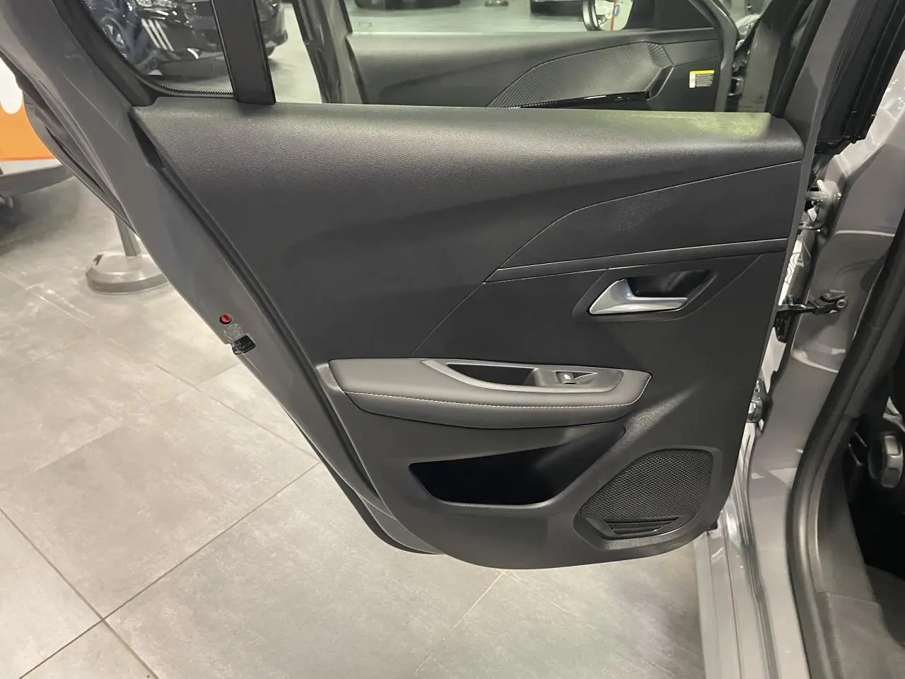 Vue intérieure de la porte arrière gauche gris selenium de la Peugeot 208 1.2i Hybrid Allure 2025 avec accoudoir et haut-parleur intégré.