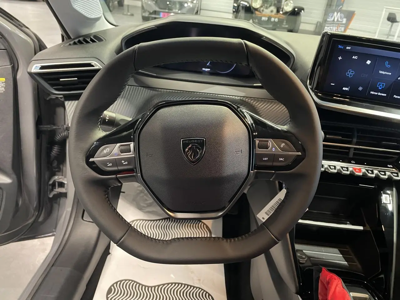 Vue rapprochée du volant cuir noir et du tableau de bord numérique de la Peugeot 208 1.2i Hybrid gris Selenium.