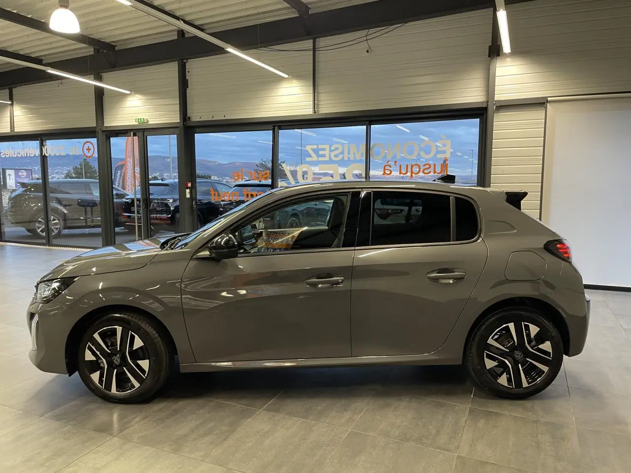 Profil droit de la Peugeot 208 hybride gris Selenium avec jantes alliage bi-tons et rétroviseurs noirs brillants.