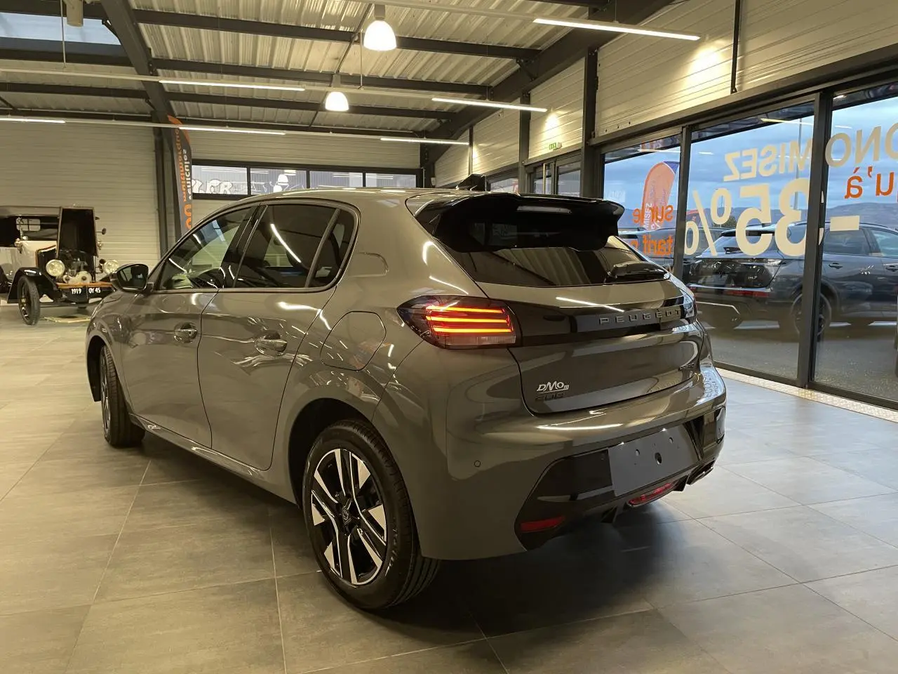 Vue 3/4 arrière droite d'une Peugeot 208 gris selenium avec feux arrière allumés en showroom.