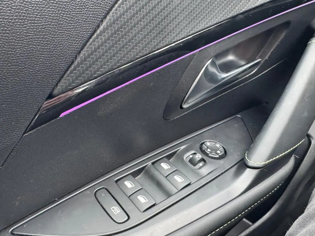 Gros plan sur la commande des vitres électriques côté conducteur d’une Peugeot 208 gris, avec insert décoratif noir et surpiqûres vertes.