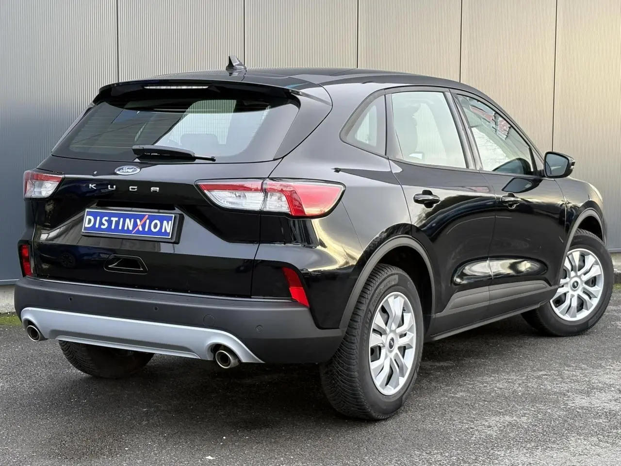 Vue 3/4 arrière droite d'un Ford Kuga 2024 noir Obsidien avec double sortie d'échappement et jantes argentées.