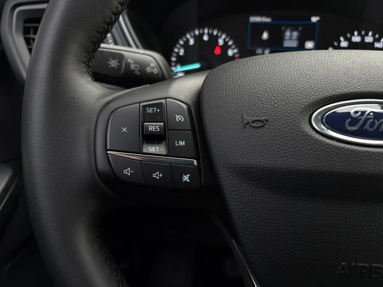 Gros plan sur le volant en cuir noir du Ford Kuga 2024 avec commandes multifonctions et logo Ford central.