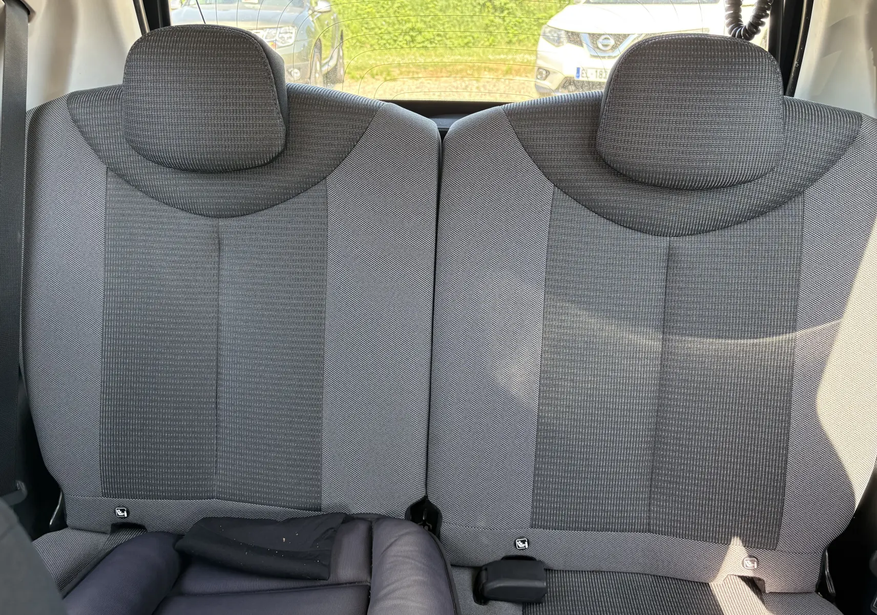 Vue intérieure des sièges arrière gris d'une Toyota Aygo MC blanche, avec appuie-têtes et ceinture de sécurité visibles.