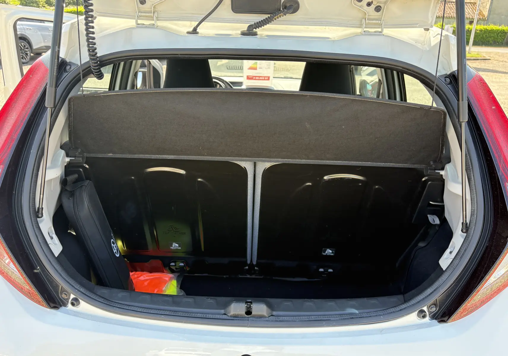 Vue arrière ouverte du coffre blanc d'une Toyota Aygo MC 2020, avec cache-bagages et accessoires visibles.
