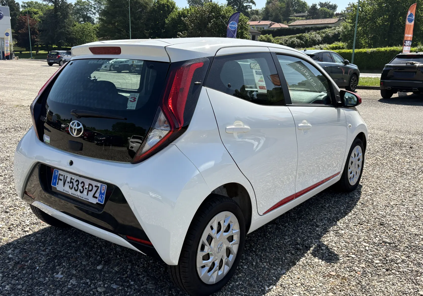 Vue 3/4 arrière droite d'une Toyota Aygo MC blanche 2020 avec toit noir et détails rouges sur le côté.