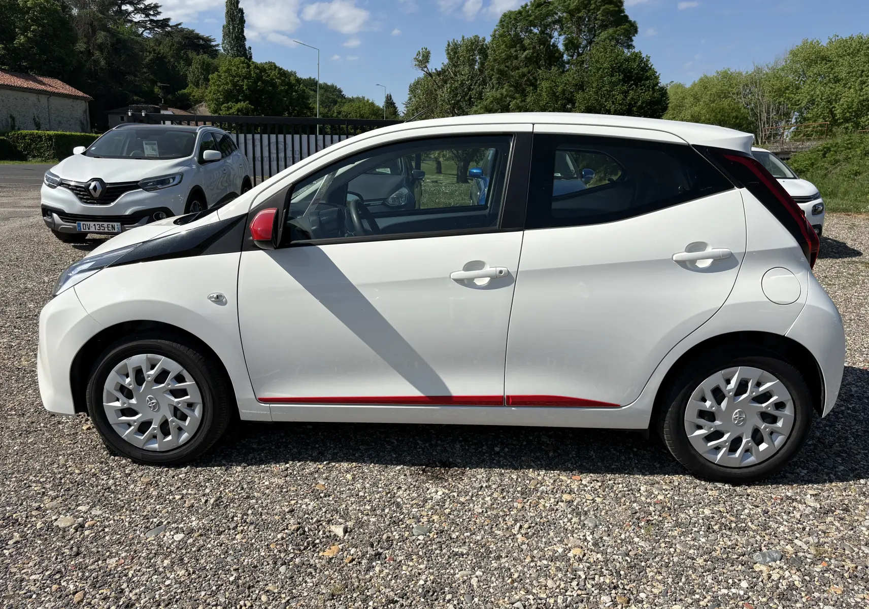 Profil droit d'une Toyota Aygo MC blanche 2020 avec rétroviseur rouge et bandeau noir sur l'aile avant.