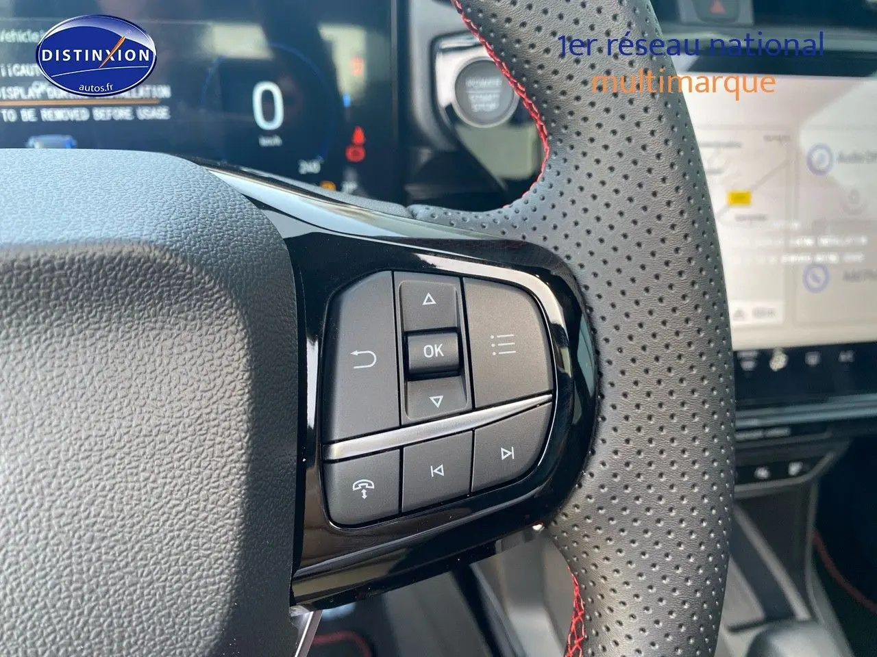 Gros plan sur les commandes du volant perforé avec surpiqûres rouges du Ford Puma rouge, tableau de bord et écran tactile en arrière-plan.
