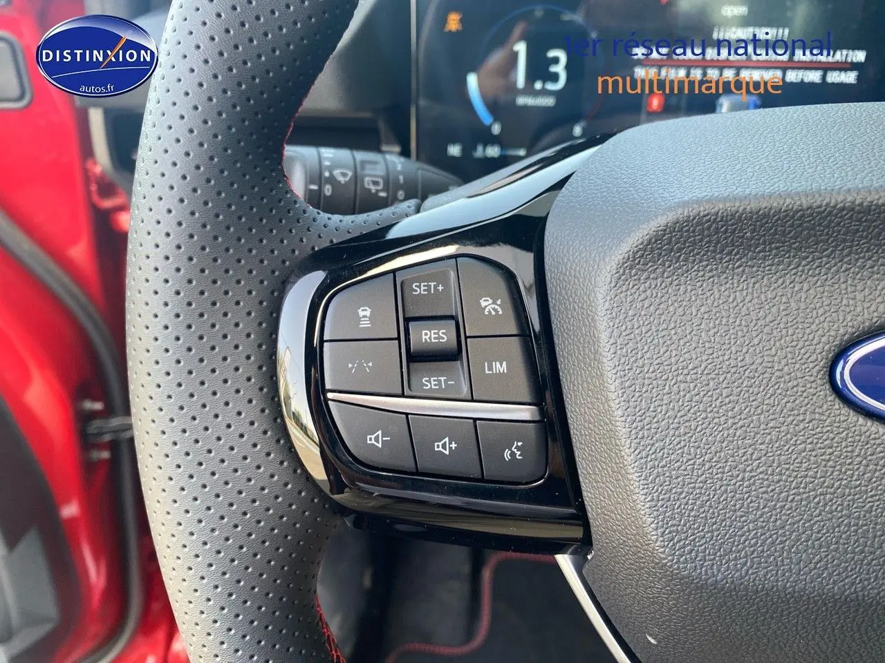 Gros plan sur les commandes multifonctions du volant perforé côté gauche d’un Ford Puma rouge métallisé.