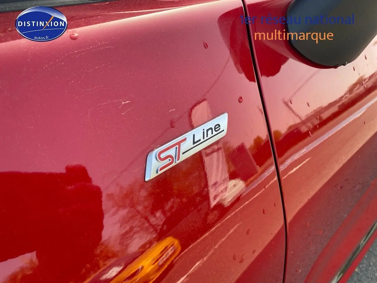 Gros plan sur l’écusson ST-Line côté gauche d’un Ford Puma rouge métallisé avec reflet et gouttes d’eau.