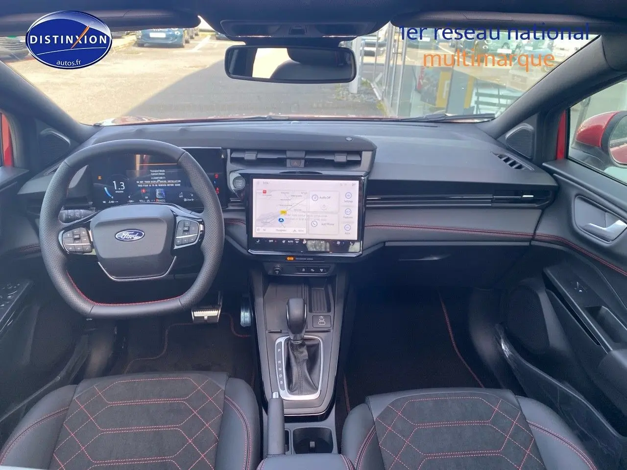Vue intérieure avant du Ford Puma rouge, montrant le volant multifonction, l’écran tactile central et les sièges sport avec surpiqûres rouges.