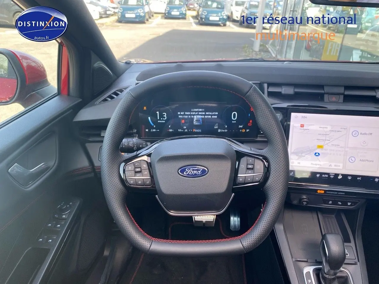 Vue intérieure centrée sur le volant perforé avec surpiqûres rouges et tableau de bord numérique de la Ford Puma rouge.