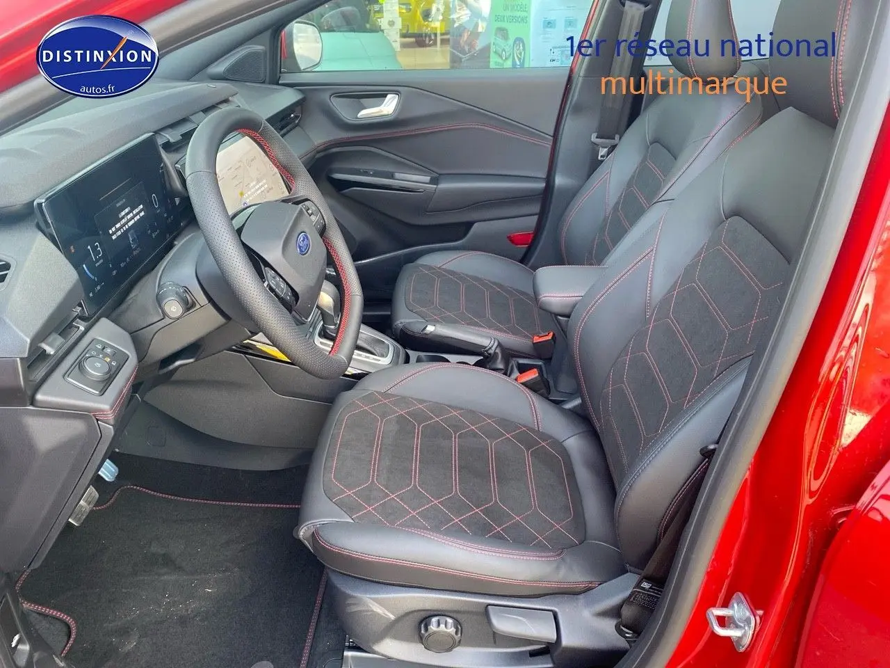 Vue intérieure côté conducteur du Ford Puma rouge, mettant en valeur les sièges sport noirs avec surpiqûres rouges et le volant multifonction.