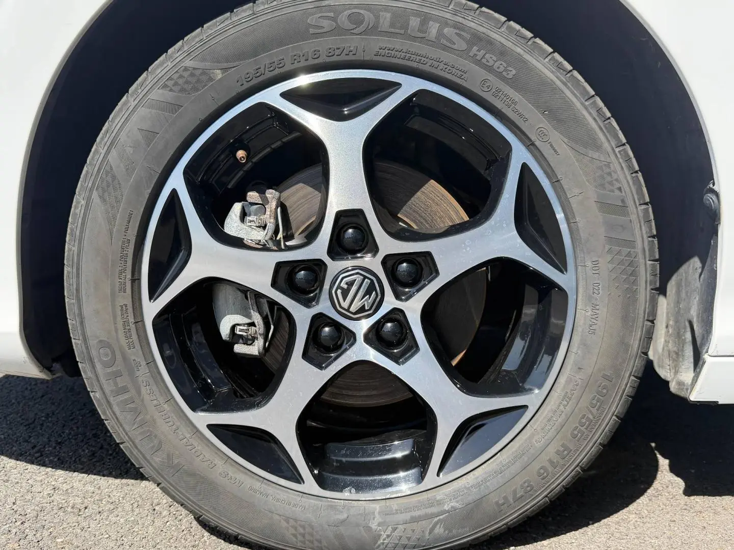 Gros plan sur la jante alu noire et argentée avec logo MG d’une MG3 blanche, vue côté roue avant droite.