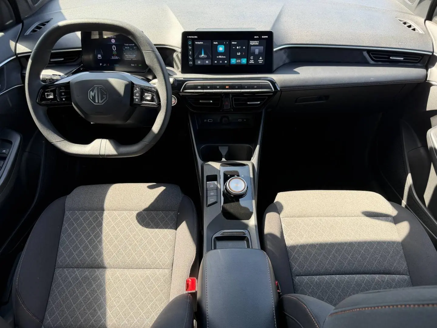 Vue intérieure avant du MG3 1.5 Hybrid+ 195ch Comfort 2025, avec tableau de bord numérique et sièges tissu gris à motifs.