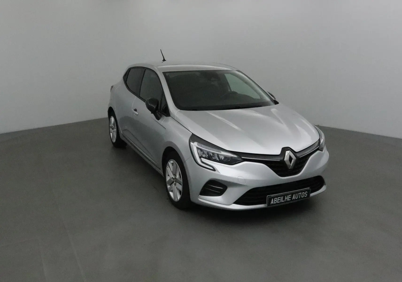 Renault Clio V gris platine vue 3/4 avant droit dans un studio, avec calandre et phares LED distinctifs.