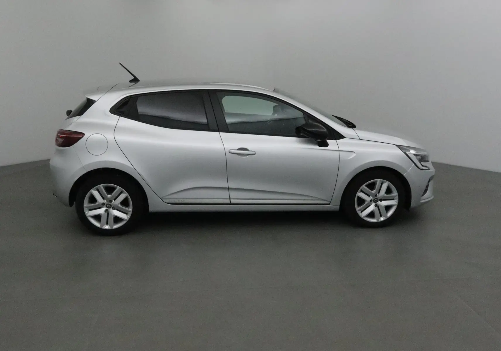 Profil côté droit d'une Renault Clio V gris platine 2021, compacte et moderne, sur fond neutre intérieur.