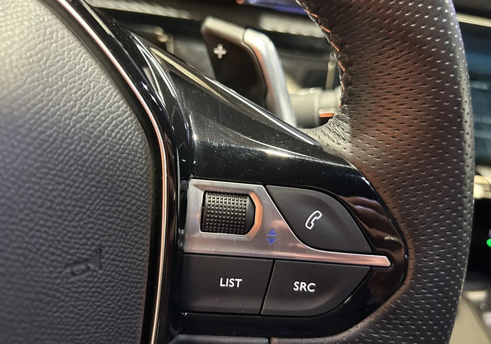 Gros plan sur les commandes gauche du volant en cuir perforé du Peugeot 508 SW Gris Artense 2024.