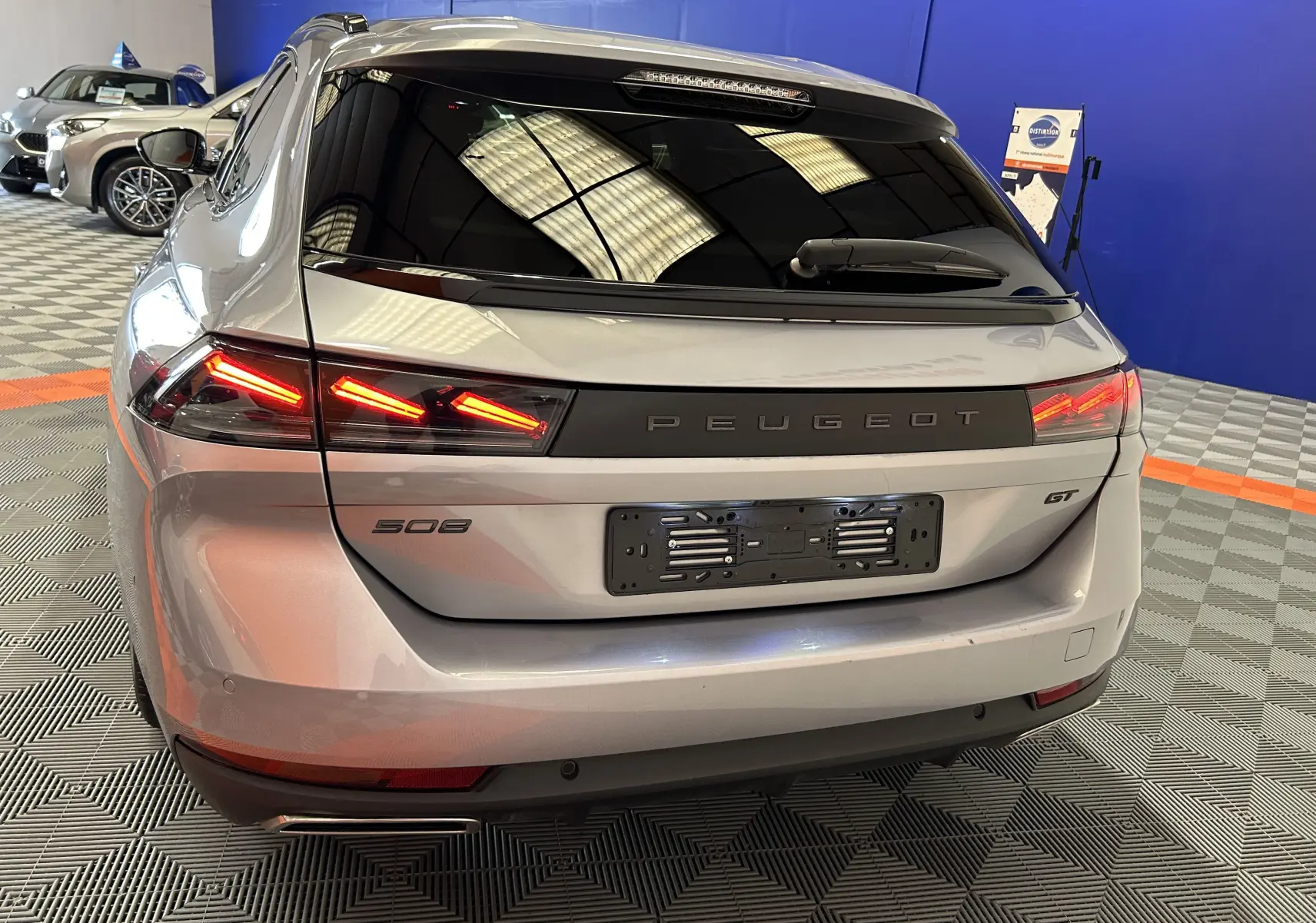 Vue arrière en léger 3/4 droit d'une Peugeot 508 SW GT gris artense avec feux LED allumés dans un showroom.