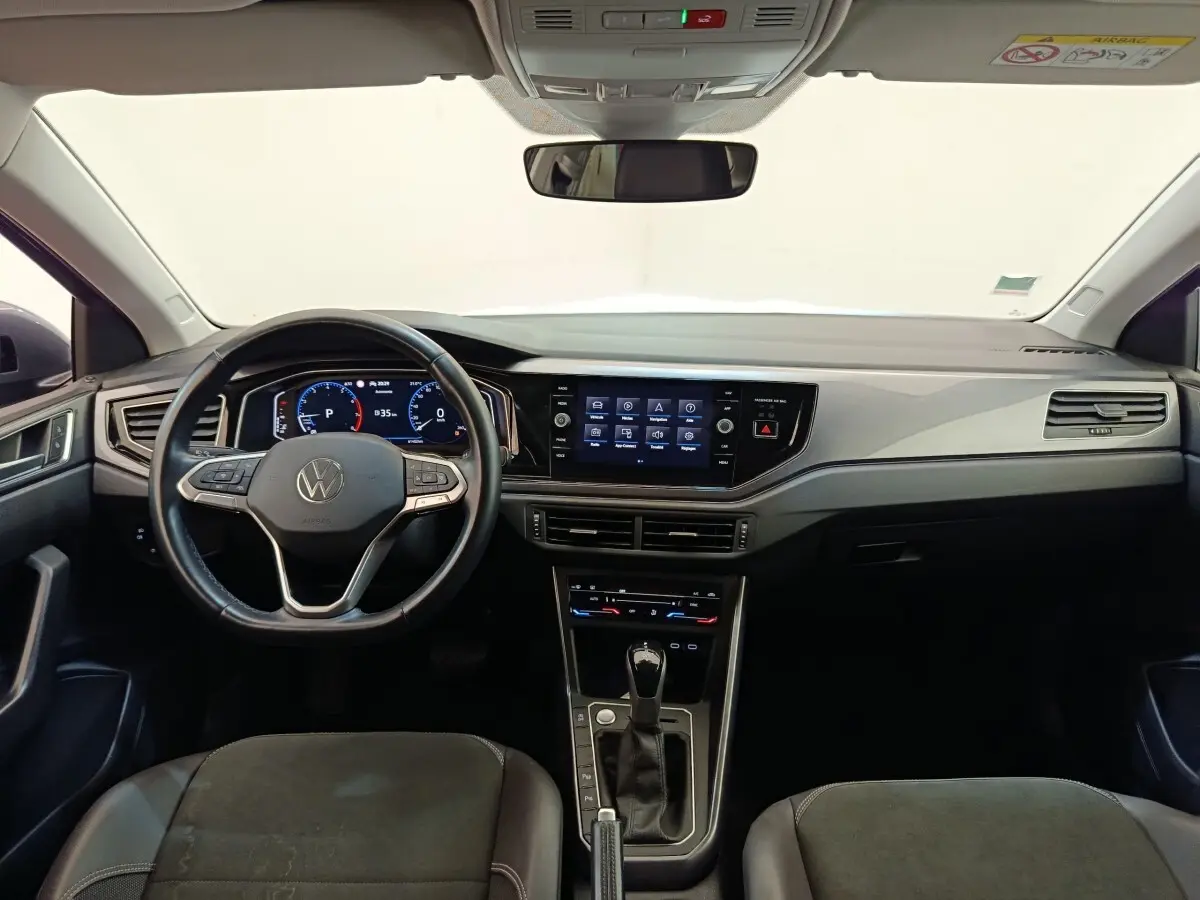 Vue intérieure frontale du tableau de bord et volant cuir noir du Volkswagen Taigo 2023, avec écran tactile central allumé.