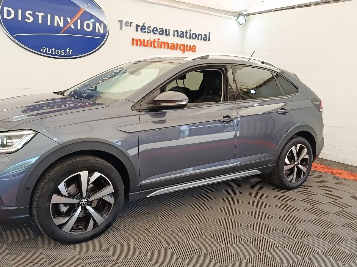 Vue de profil côté gauche du Volkswagen Taigo gris foncé avec jantes alliage et barres de toit chromées en intérieur showroom.