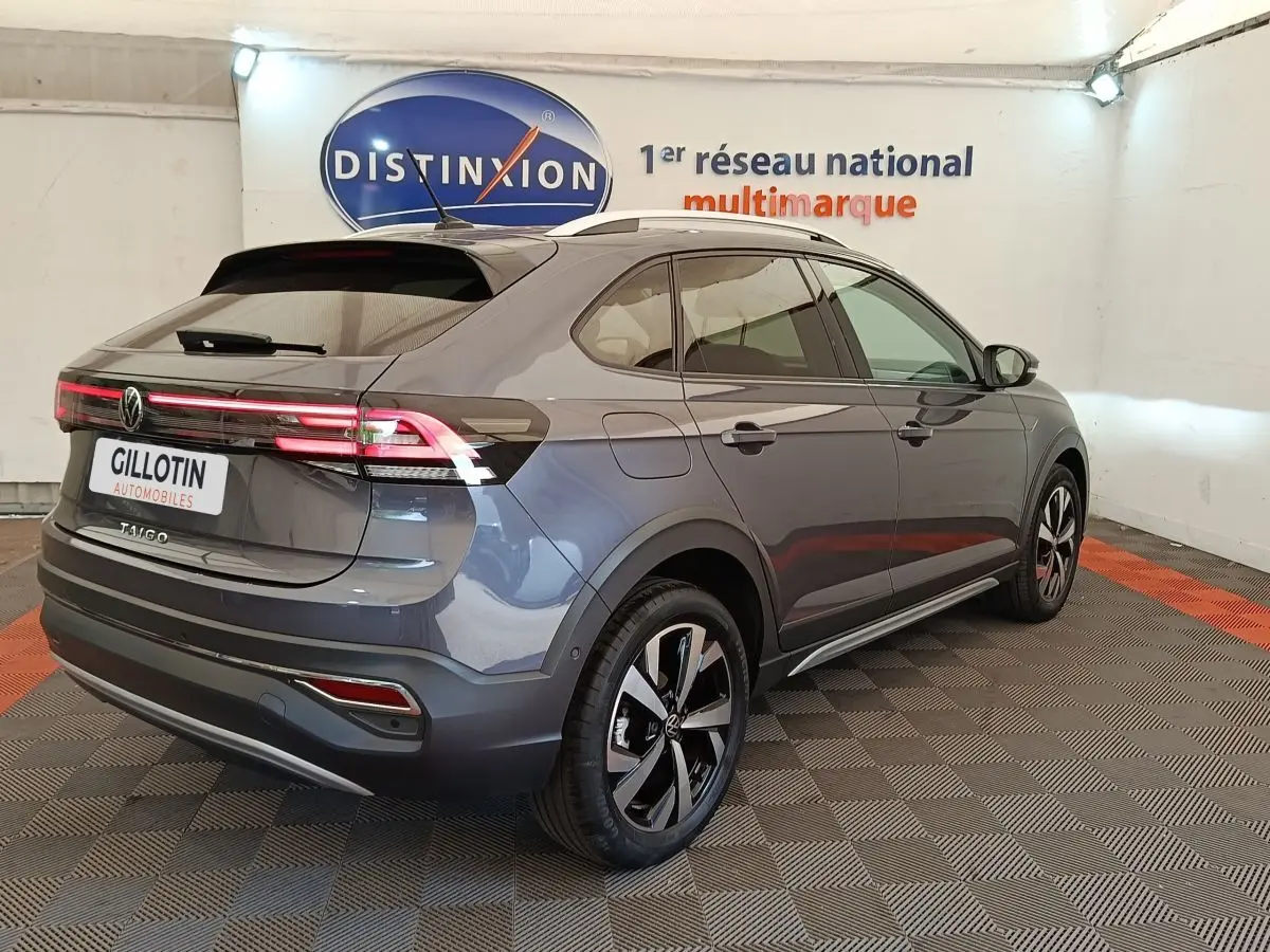 Volkswagen Taigo gris foncé en 3/4 arrière droit, avec feux arrière LED allumés dans un showroom.