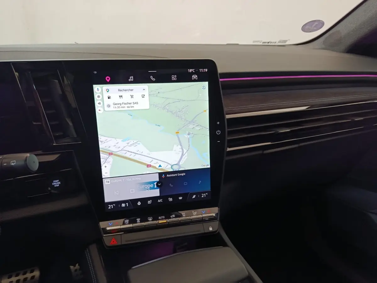 Vue intérieure du tableau de bord du Renault Austral gris clair, avec écran tactile central affichant la navigation et éclairage d’ambiance violet.