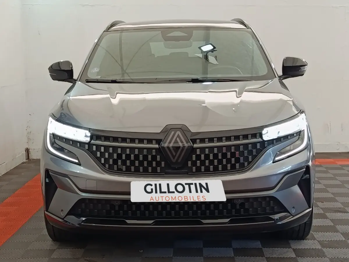 Vue frontale du Renault Austral gris clair avec calandre à damier et phares LED allumés dans un showroom.
