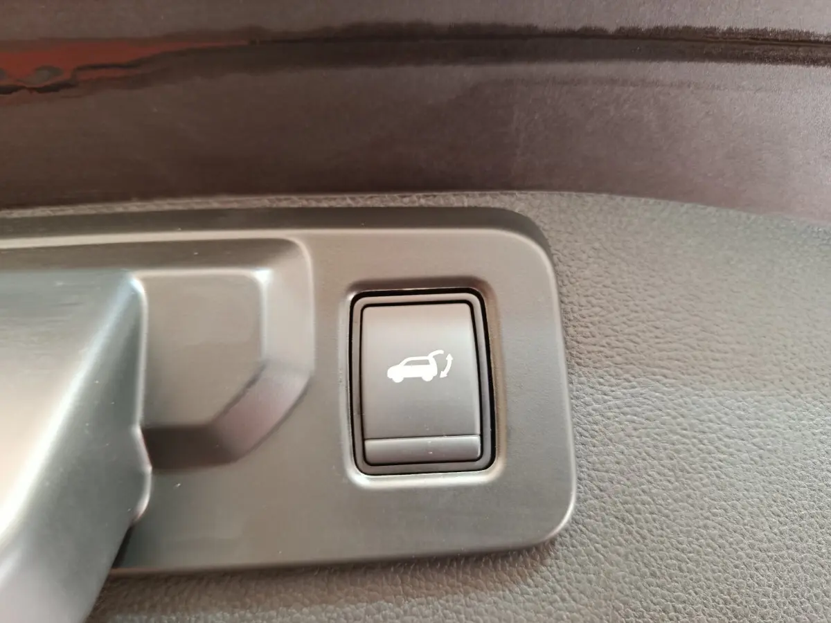 Bouton noir d'ouverture électrique du coffre sur panneau intérieur gris d'un Renault Austral gris clair, vue rapprochée.