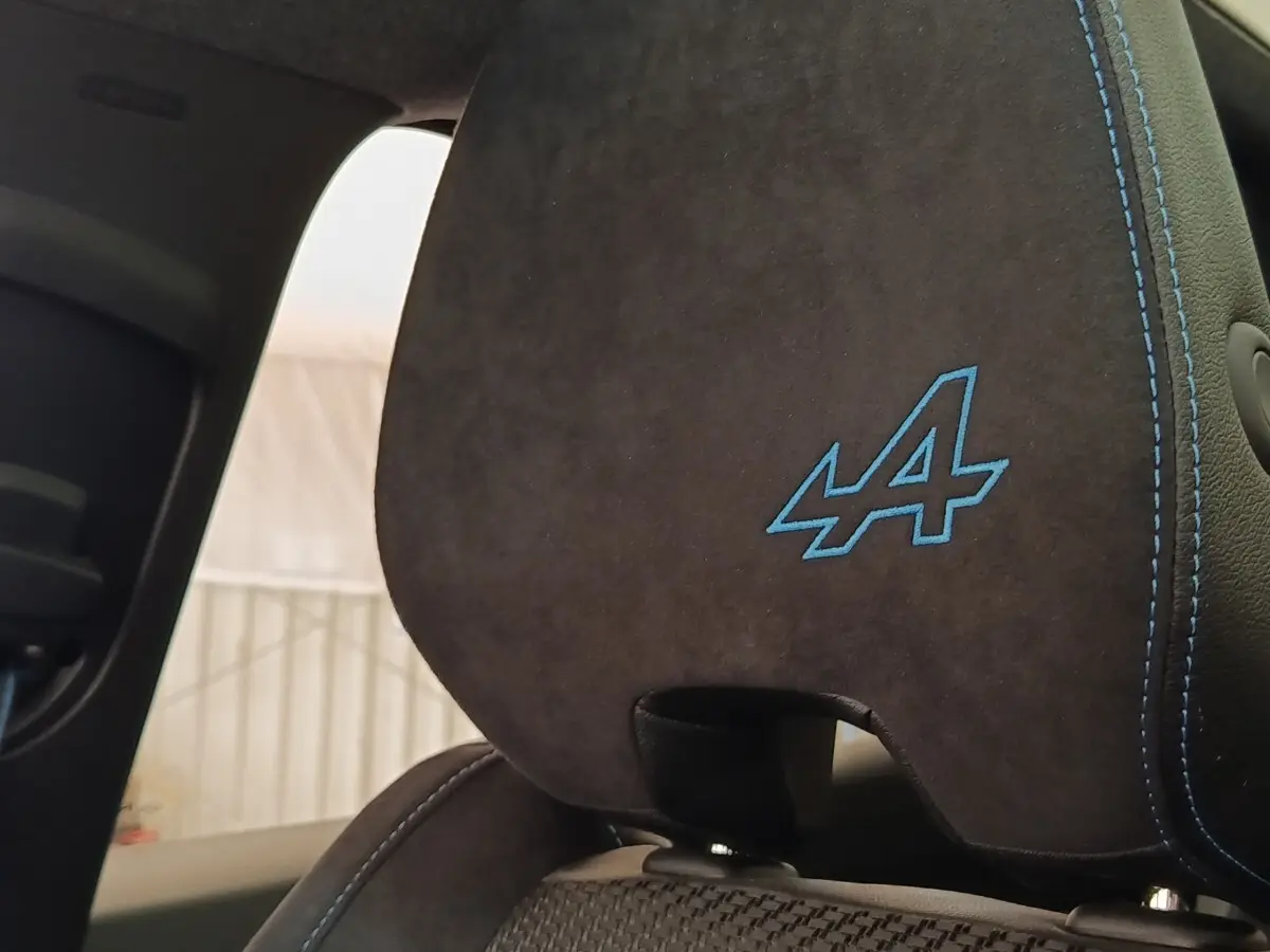 Gros plan sur l’appui-tête arrière en suédine noire avec logo Alpine bleu et surpiqûres assorties.