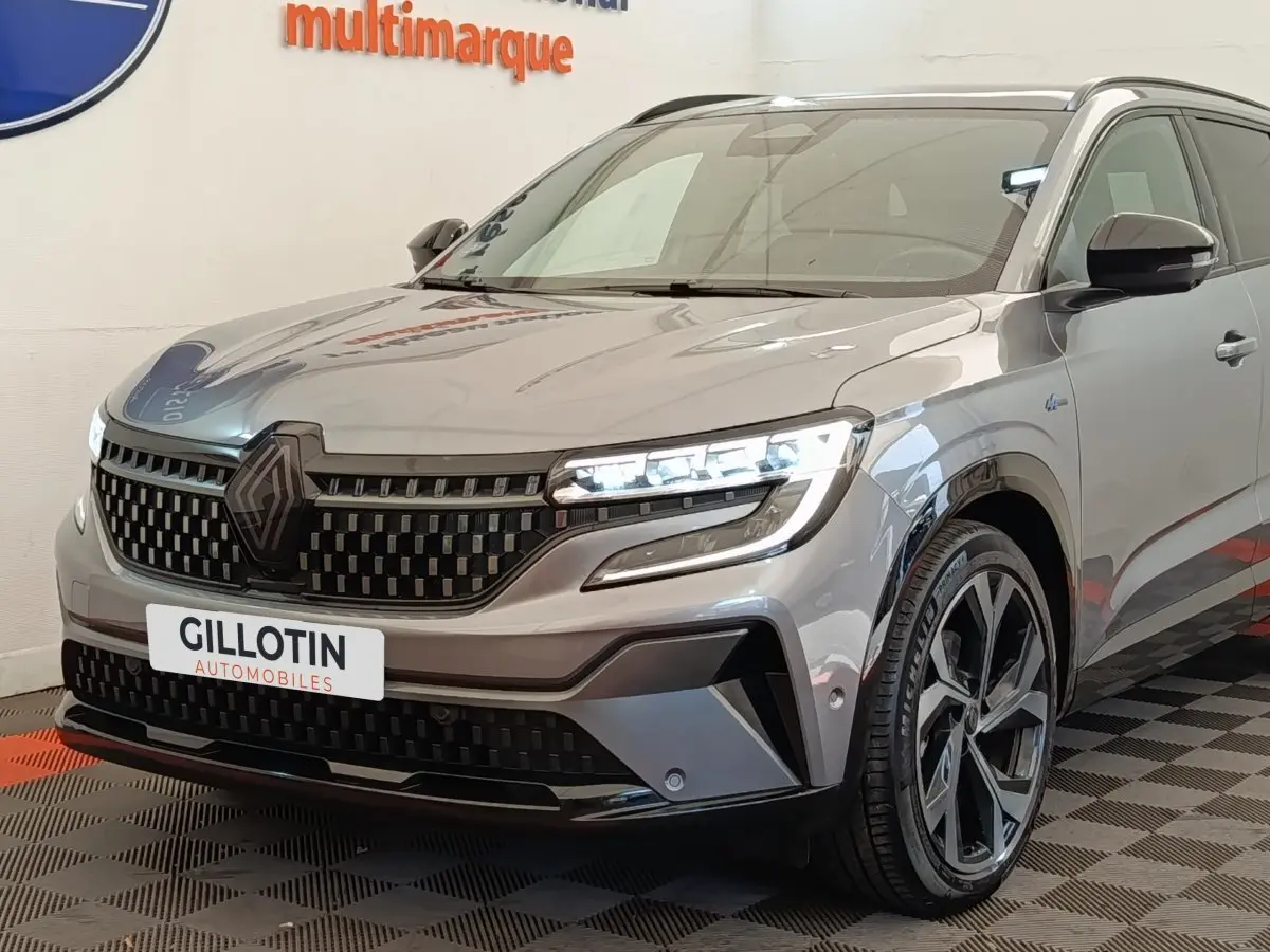 Vue 3/4 avant droite du Renault Austral gris clair avec calandre noire et phares LED allumés en intérieur showroom.