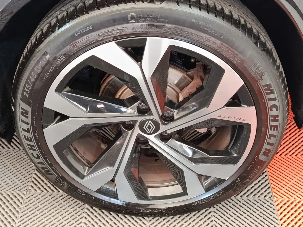 Gros plan sur la jante aluminium bicolore avec logo Renault et inscription Alpine sur un Renault Austral gris clair.