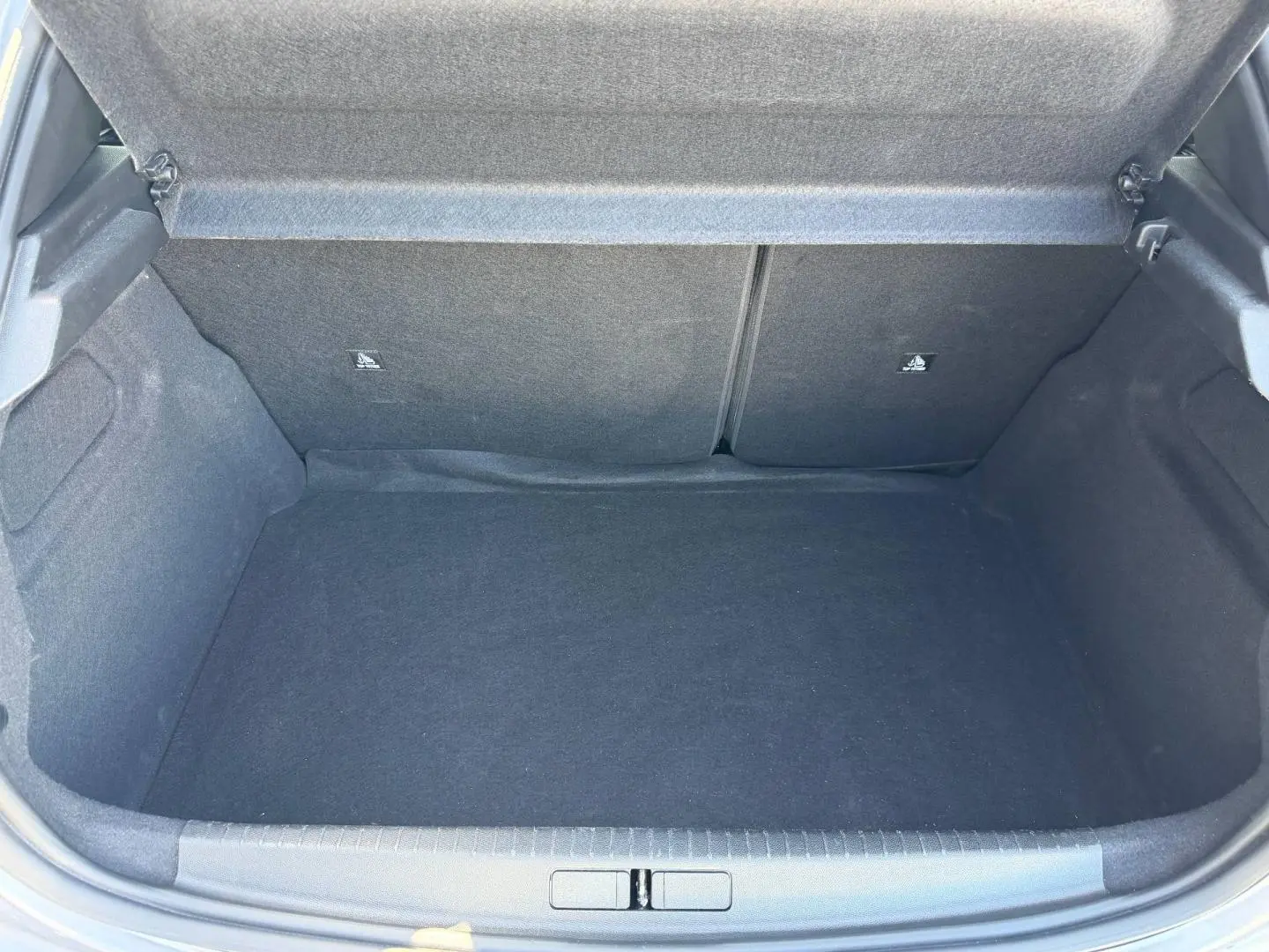 Coffre ouvert de la Peugeot 208 1.2 100ch Allure gris Artense, montrant l'espace de chargement vide et la banquette arrière rabattable.