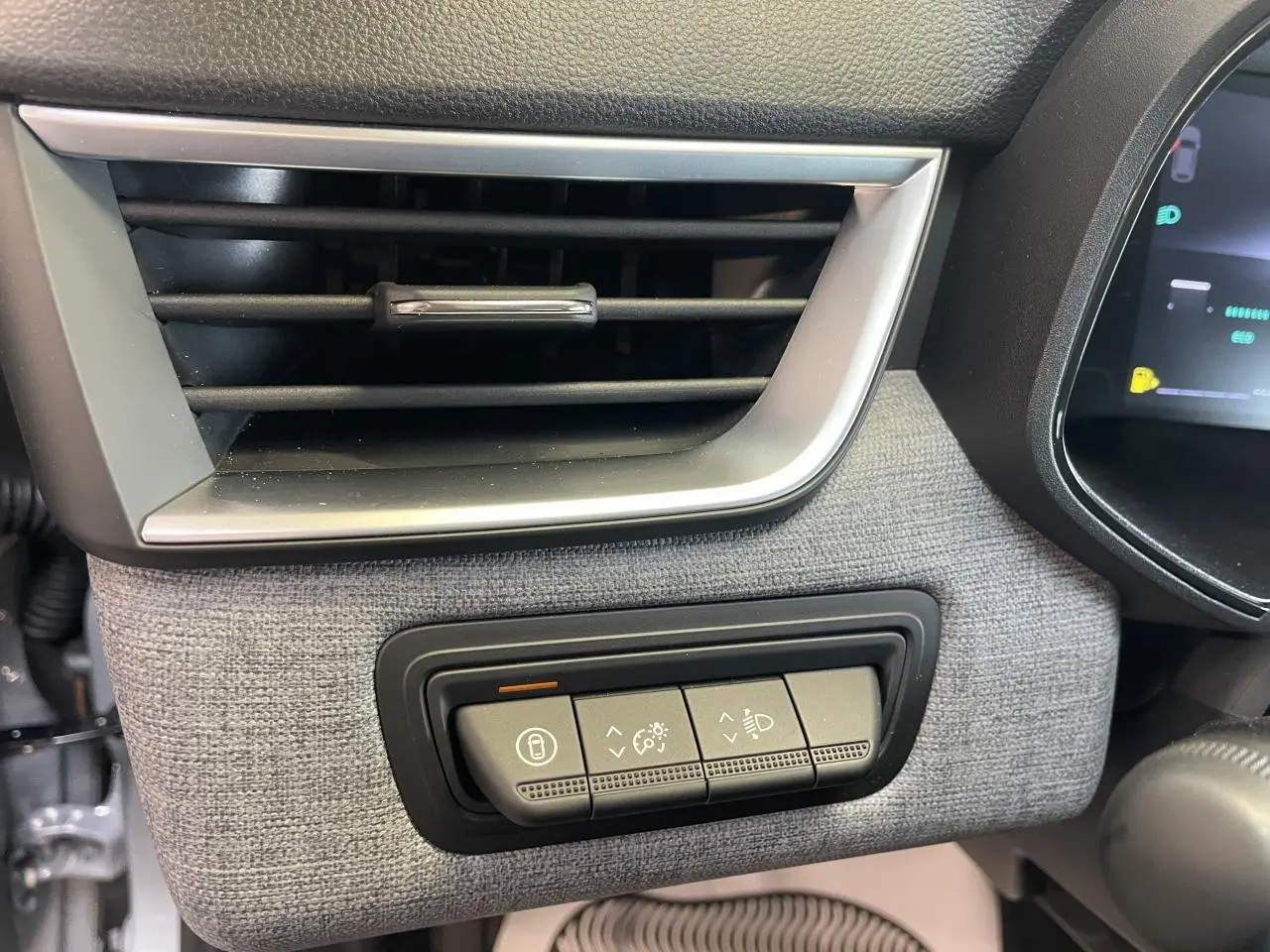 Détail de la console côté gauche avec aérateur chrome satiné et commandes d’éclairage sur tissu gris dans Renault Clio 2025.