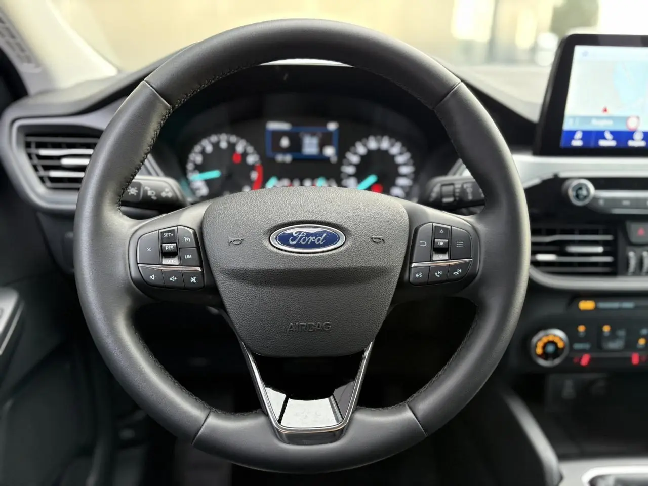 Vue rapprochée du volant en cuir multifonctions du Ford Kuga 2024 avec tableau de bord et écran GPS tactile en arrière-plan.