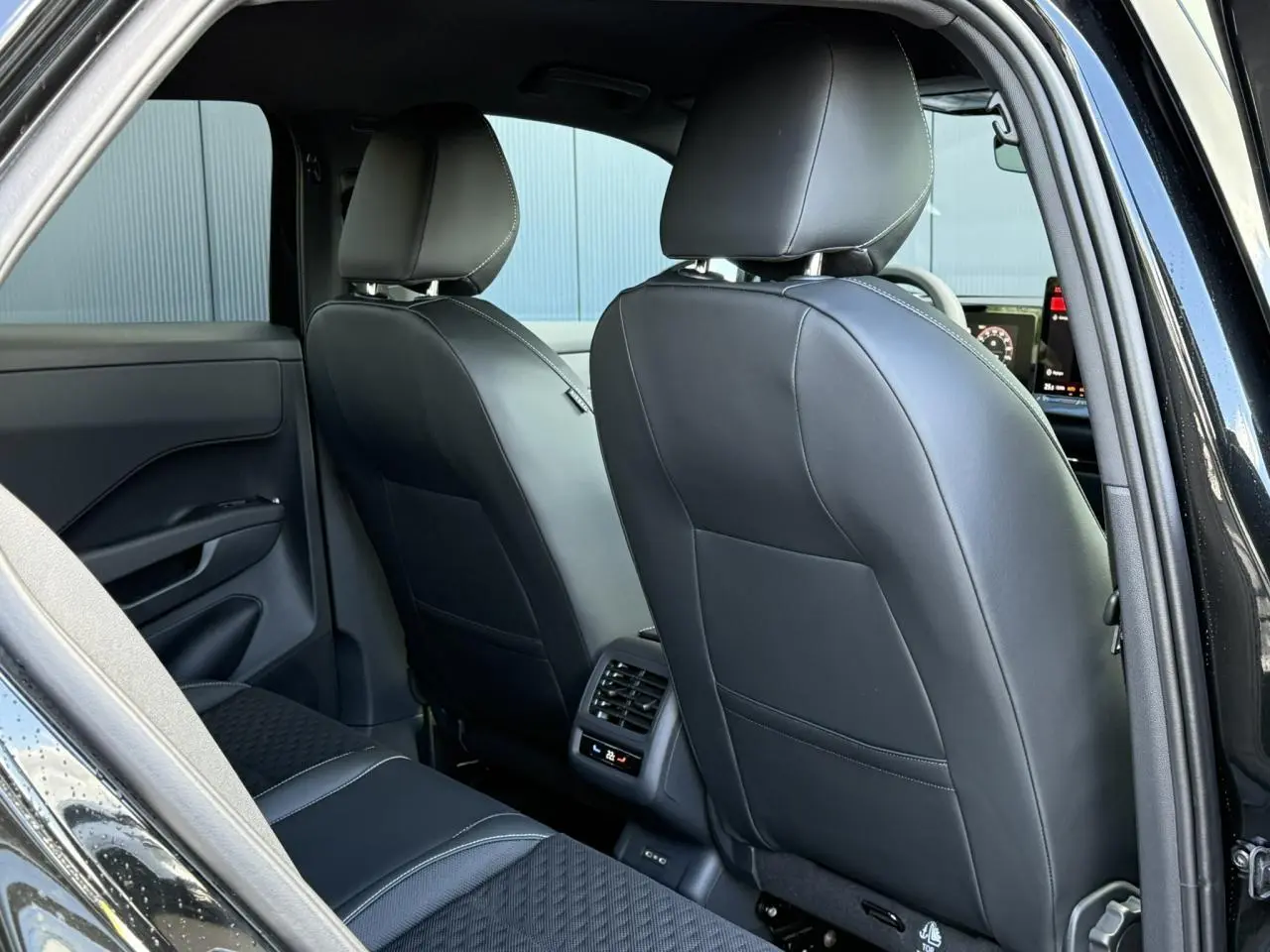 Vue arrière intérieure du Volkswagen T-Roc 2026 noir Ébène, sièges avant en cuir noir et ventilation arrière visible.