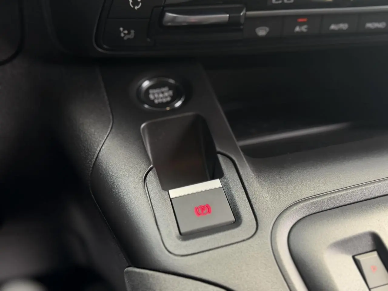 Gros plan sur la console centrale du Peugeot Rifter avec bouton frein de stationnement électrique allumé en rouge.