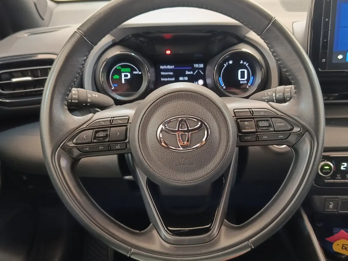 Vue rapprochée du volant cuir noir de la Toyota Yaris Hybride 116h 2022 avec tableau de bord numérique allumé.