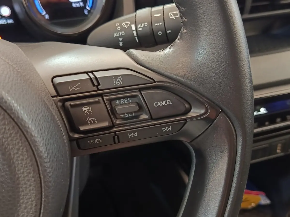 Gros plan sur le côté droit du volant cuir noir de la Toyota Yaris Hybride 116h avec commandes multifonctions intégrées.