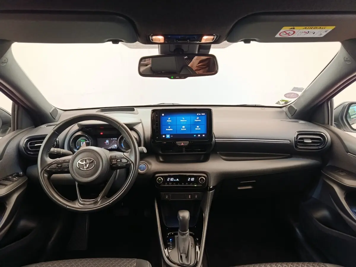 Vue intérieure frontale du tableau de bord noir de la Toyota Yaris Hybride 116h avec écran tactile central et volant multifonctions.
