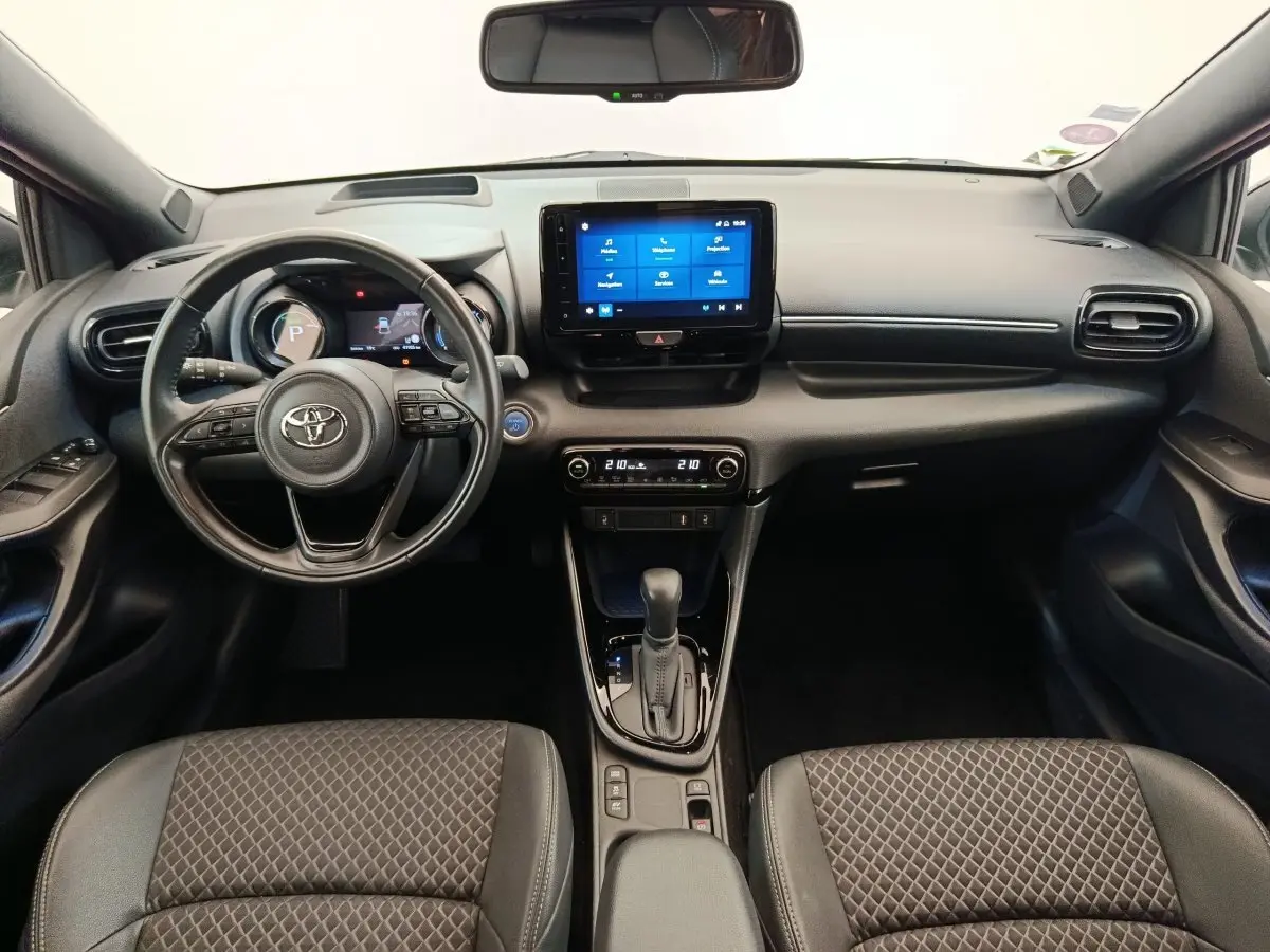 Vue intérieure avant de la Toyota Yaris Hybride 116h 2022, tableau de bord noir avec écran tactile central et volant cuir.