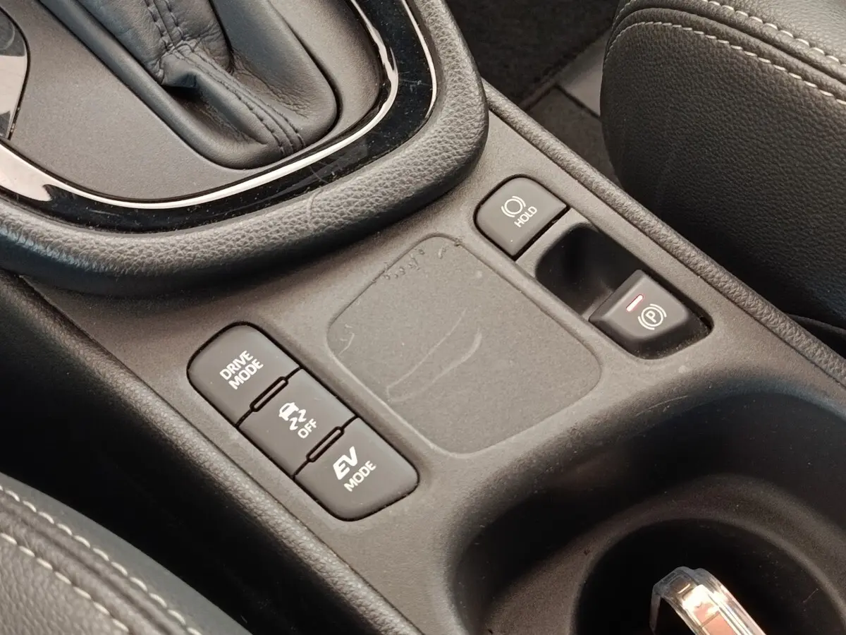 Gros plan sur la console centrale noire de la Toyota Yaris Hybride 116h avec boutons mode conduite et frein électrique.