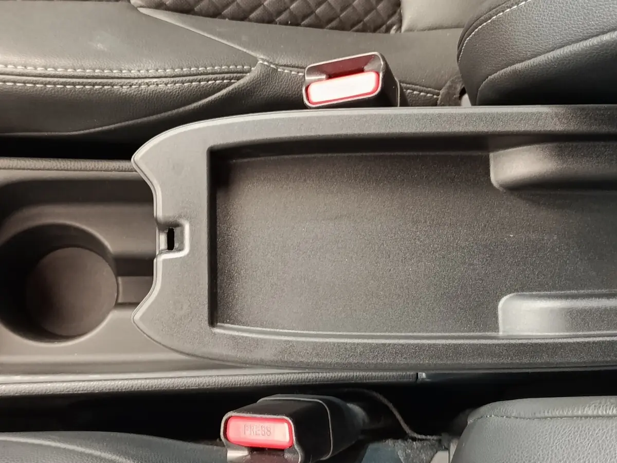 Vue rapprochée de la console centrale noire avec porte-gobelet et ceintures de sécurité rouges dans une Toyota Yaris blanche hybride.