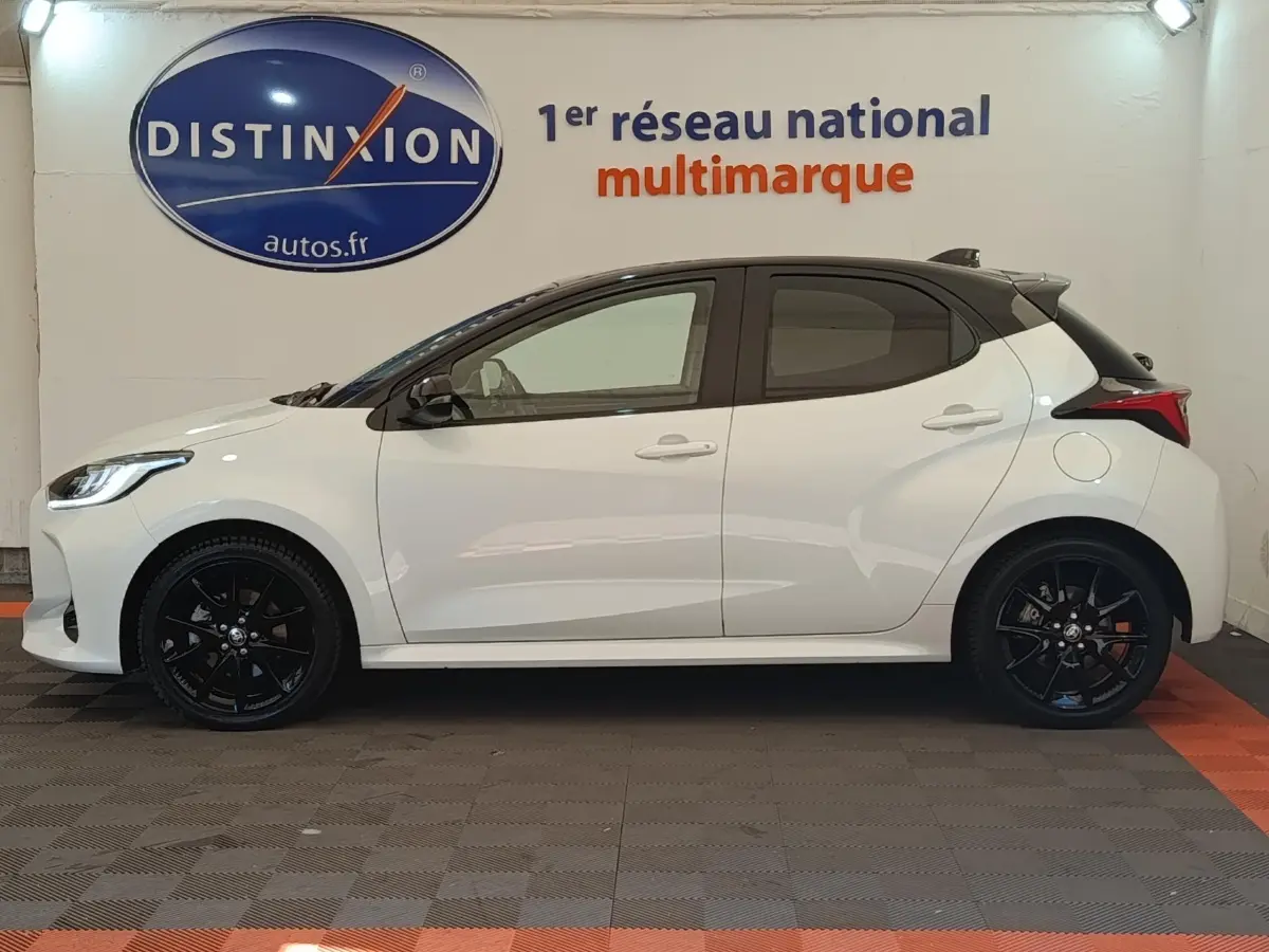 Profil droit d'une Toyota Yaris Hybride 116h Collection blanche avec jantes noires et toit noir en intérieur showroom.
